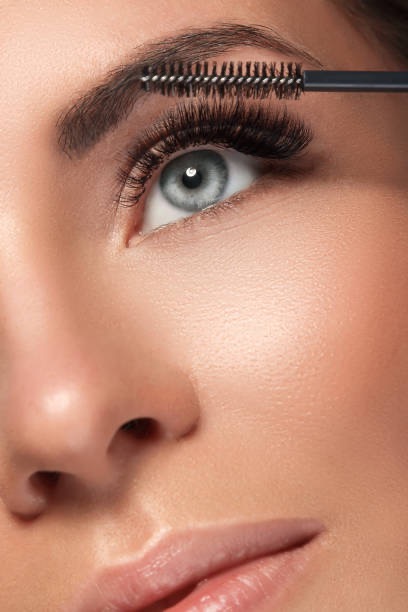 Frau mit blauen Augen und langen Wimpern beim Auftragen von Mascara